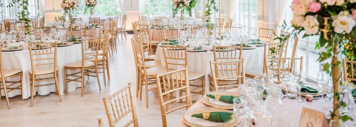 Elegant indoor wedding reception with gold Chiavari chairs and floral centrepieces