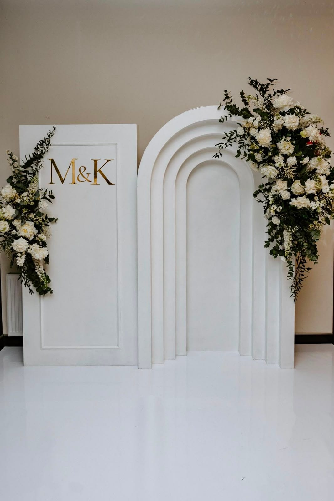 White arch backdrop with white florals and 'M&K' signage